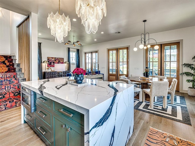 kitchen featuring french doors, a kitchen island, light stone countertops, decorative light fixtures, and light hardwood / wood-style floors