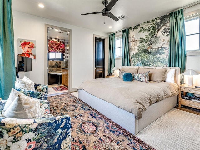 bedroom featuring hardwood / wood-style floors, ceiling fan, connected bathroom, and multiple windows