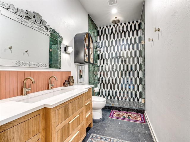 bathroom featuring a tile shower, vanity, and toilet