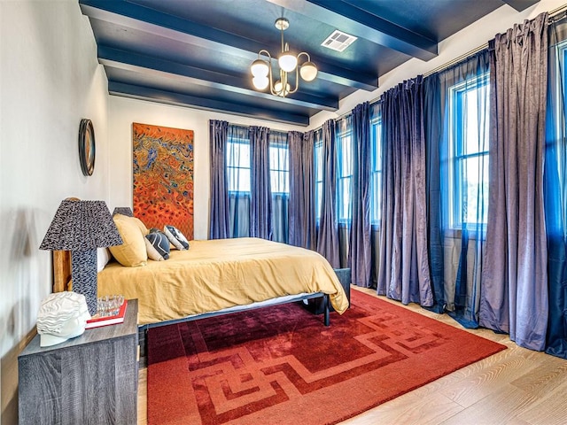 bedroom featuring multiple windows, a chandelier, beamed ceiling, and wood-type flooring