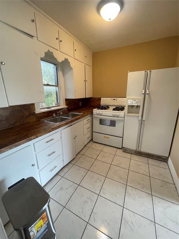 kitchen with white cabinetry, sink, light tile patterned flooring, and white appliances