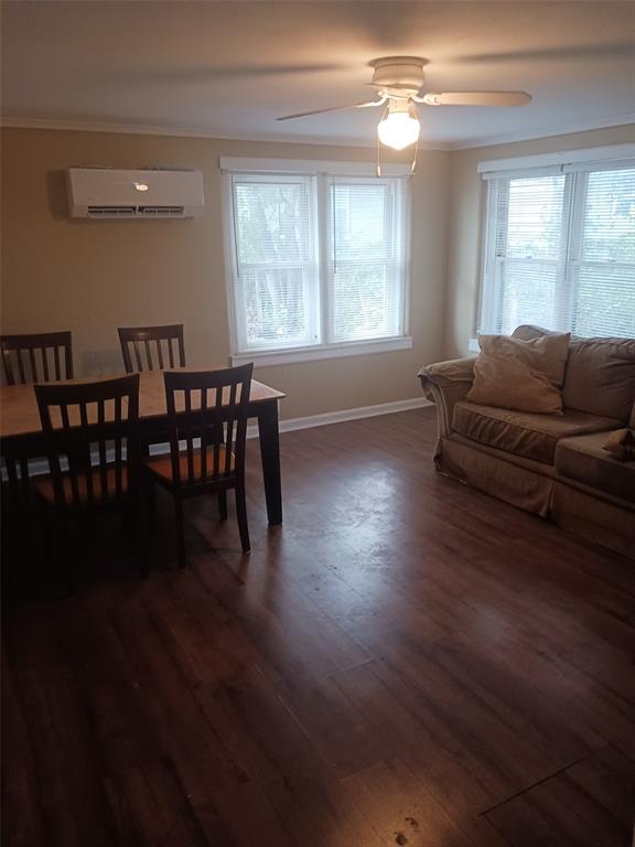 dining room featuring a healthy amount of sunlight, a wall mounted AC, dark wood-type flooring, and ceiling fan