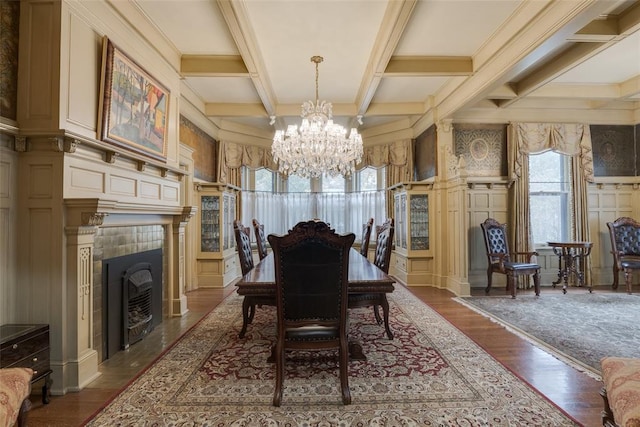 dining area featuring hardwood / wood-style floors, an inviting chandelier, coffered ceiling, beam ceiling, and a tiled fireplace