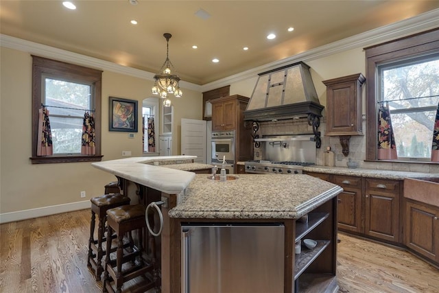 kitchen featuring crown molding, an island with sink, light hardwood / wood-style floors, decorative backsplash, and custom range hood