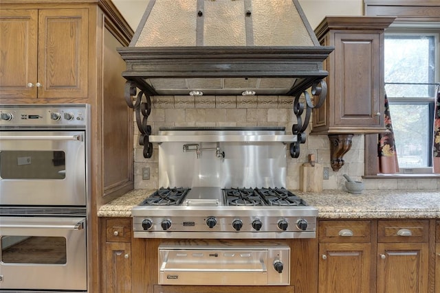 kitchen featuring backsplash, light stone countertops, custom range hood, and appliances with stainless steel finishes