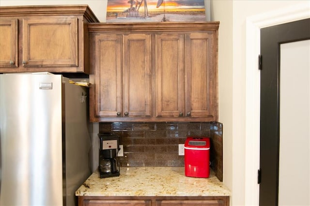 kitchen featuring decorative backsplash, stainless steel refrigerator, and light stone counters