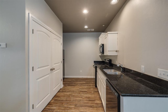 kitchen featuring sink, dark stone countertops, wood-type flooring, white cabinets, and appliances with stainless steel finishes