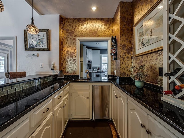 kitchen with backsplash, sink, hanging light fixtures, stainless steel fridge, and dark stone countertops