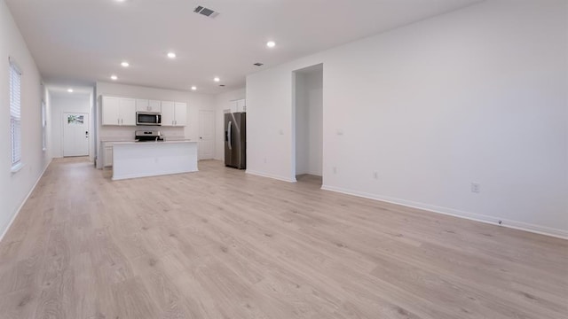 kitchen featuring stainless steel appliances, white cabinetry, visible vents, open floor plan, and a center island