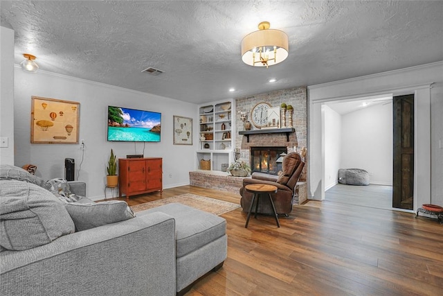 living room with built in shelves, wood-type flooring, a textured ceiling, and a brick fireplace