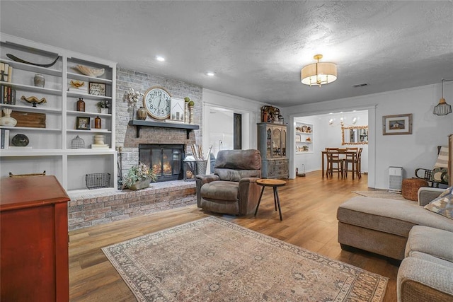 living room with hardwood / wood-style flooring, built in shelves, a textured ceiling, and a brick fireplace