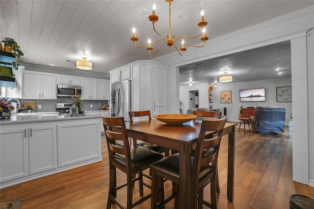 dining area with crown molding, sink, dark wood-type flooring, and an inviting chandelier