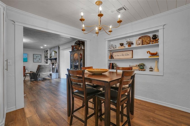 dining space featuring built in shelves, dark hardwood / wood-style floors, crown molding, and a notable chandelier