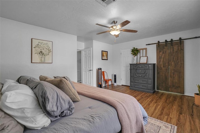 bedroom with ceiling fan, a barn door, dark hardwood / wood-style flooring, and a textured ceiling