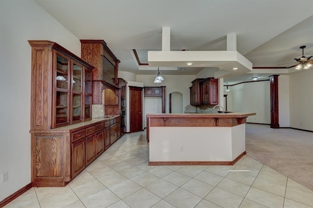 kitchen featuring ceiling fan, kitchen peninsula, pendant lighting, light colored carpet, and a tray ceiling