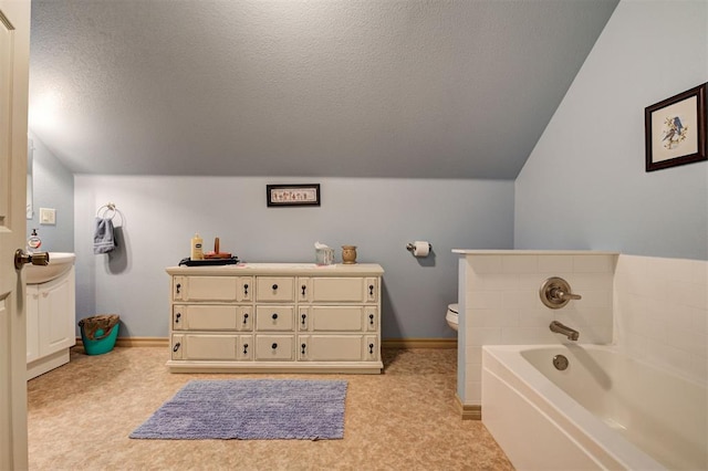 bathroom with a textured ceiling, vanity, vaulted ceiling, a bath, and toilet