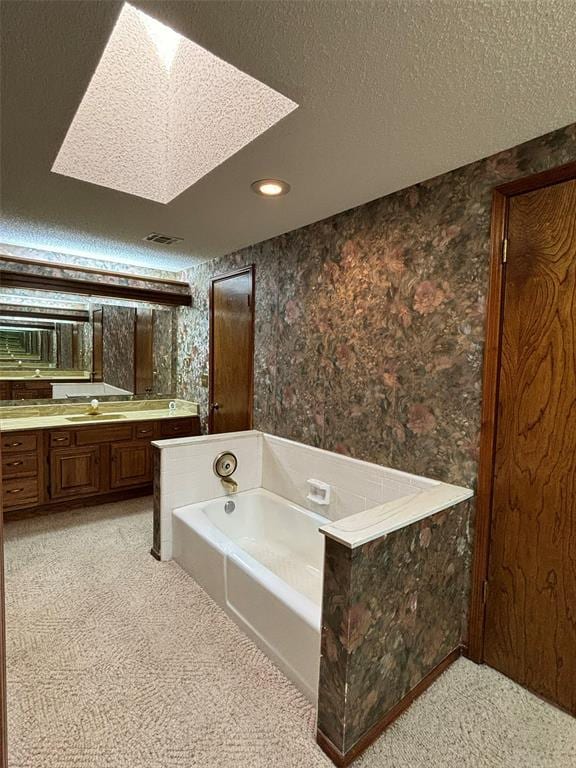 bathroom with vanity, a bath, a textured ceiling, and a skylight