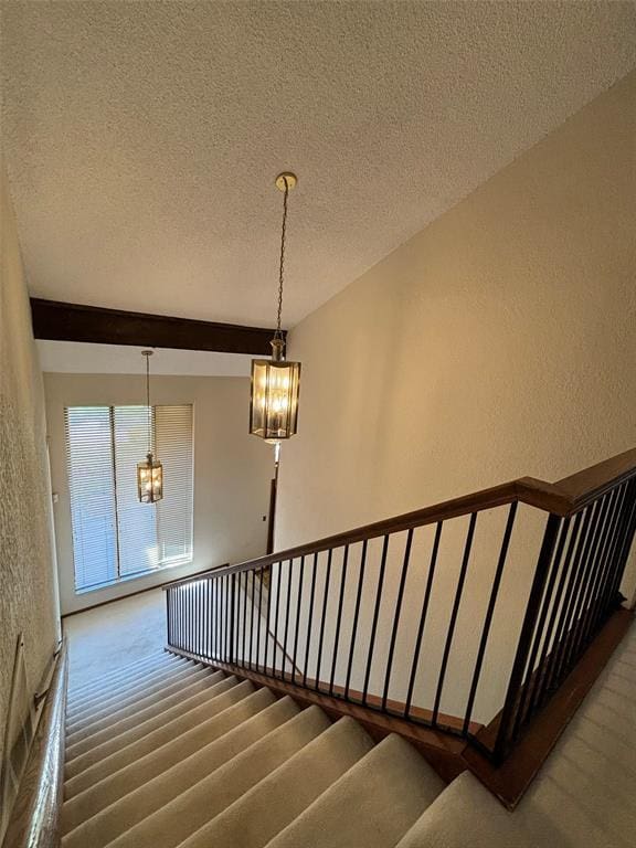 stairs with hardwood / wood-style flooring, beam ceiling, a textured ceiling, and an inviting chandelier