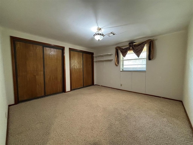 unfurnished bedroom featuring multiple closets and light colored carpet