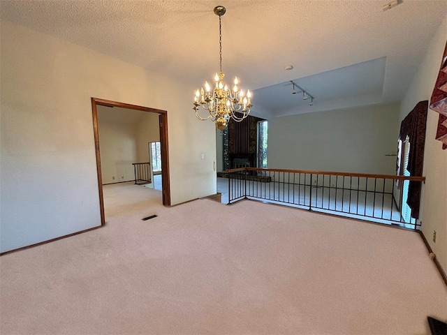 carpeted spare room featuring a textured ceiling, track lighting, and an inviting chandelier