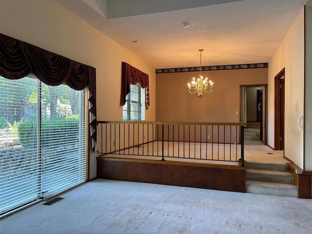 empty room featuring carpet, a healthy amount of sunlight, a textured ceiling, and a notable chandelier