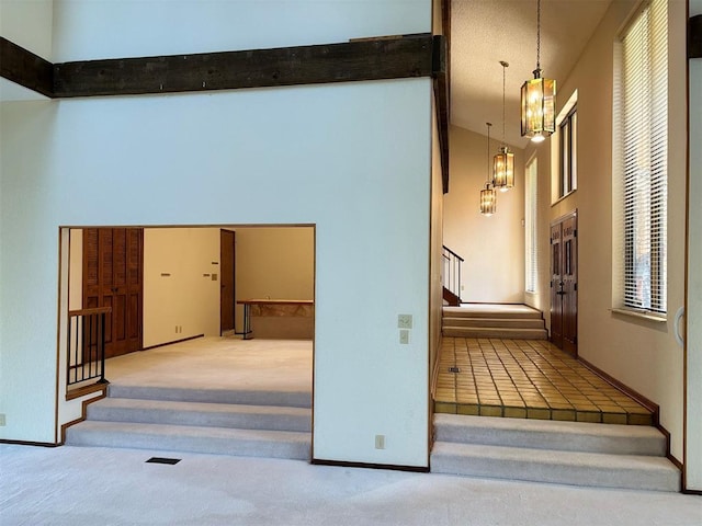 interior space featuring carpet flooring, a high ceiling, a notable chandelier, and beam ceiling