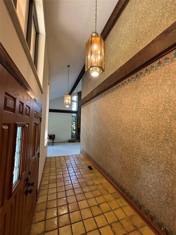 entryway featuring a textured ceiling, an inviting chandelier, high vaulted ceiling, beamed ceiling, and tile patterned flooring