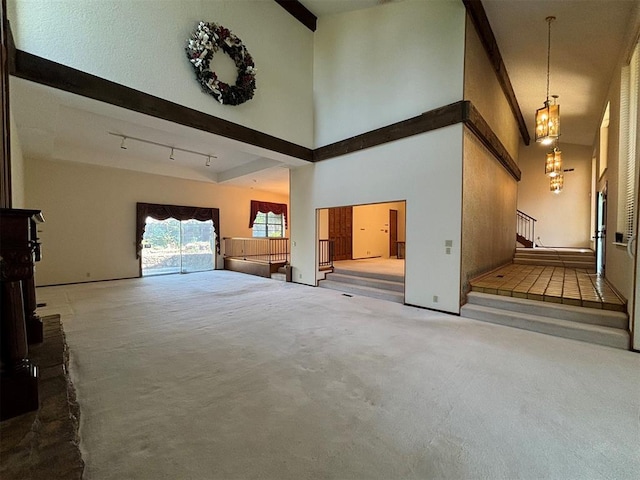 unfurnished living room with an inviting chandelier, light carpet, a high ceiling, and track lighting