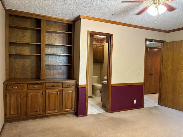 interior space with a textured ceiling, ensuite bath, ceiling fan, and crown molding