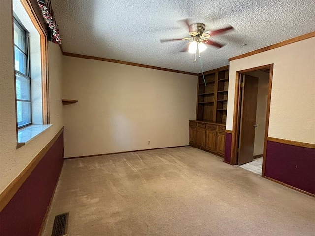 empty room with ceiling fan, crown molding, a textured ceiling, and light carpet