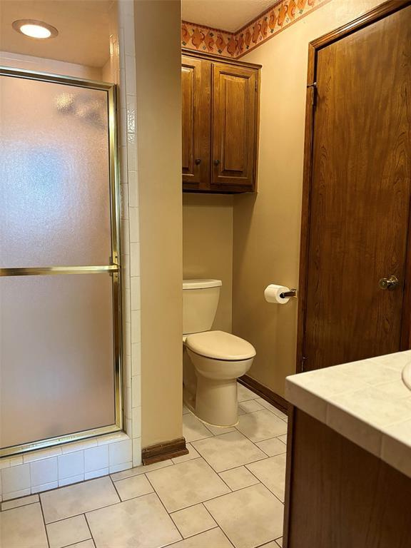 bathroom featuring tile patterned floors, vanity, toilet, and a shower with door