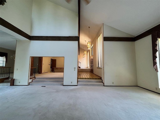 carpeted empty room with high vaulted ceiling and a chandelier