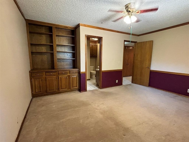 unfurnished bedroom with ceiling fan, crown molding, ensuite bathroom, light colored carpet, and a textured ceiling