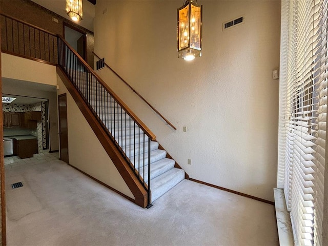 stairway with carpet, a towering ceiling, and an inviting chandelier