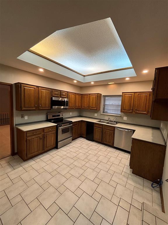 kitchen with appliances with stainless steel finishes, a textured ceiling, a tray ceiling, and sink