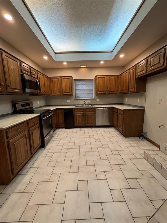 kitchen featuring sink, stainless steel appliances, a textured ceiling, a tray ceiling, and light tile patterned floors