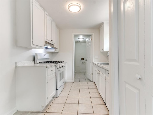 kitchen with white gas stove, white cabinets, light tile patterned floors, and sink