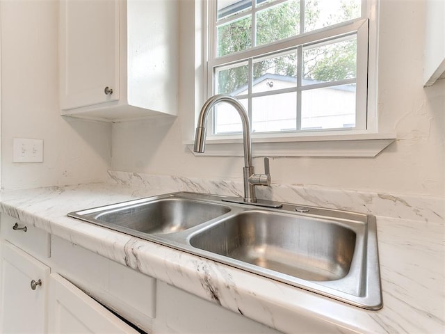 room details featuring white cabinets, light stone countertops, and sink