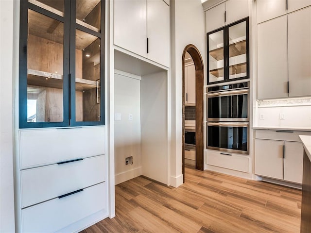 kitchen featuring white cabinets, decorative backsplash, double oven, and light hardwood / wood-style flooring