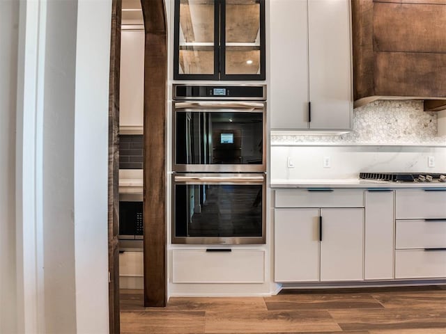 kitchen featuring dark hardwood / wood-style floors, decorative backsplash, white cabinetry, and double oven