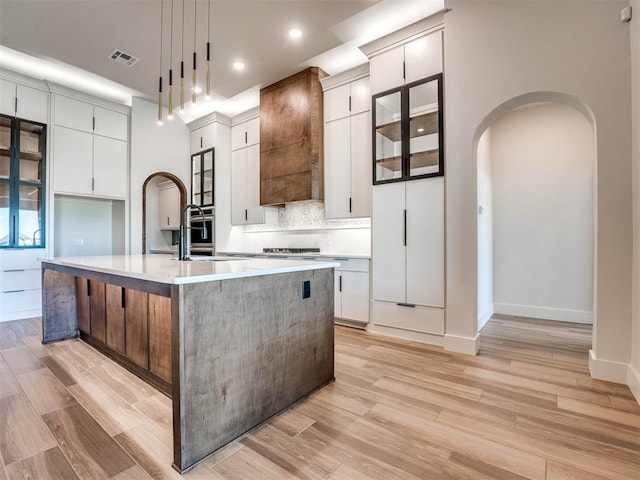 kitchen with pendant lighting, white cabinetry, light hardwood / wood-style flooring, and a kitchen island with sink