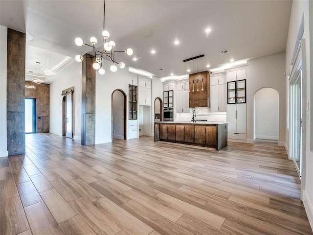 kitchen featuring a large island with sink, white cabinetry, oven, and light wood-type flooring