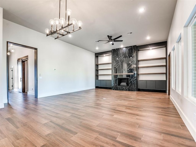 unfurnished living room featuring a barn door, light hardwood / wood-style flooring, a fireplace, and ceiling fan with notable chandelier