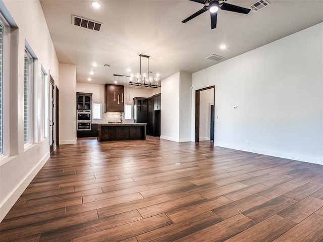 unfurnished living room featuring ceiling fan with notable chandelier, dark hardwood / wood-style flooring, and sink