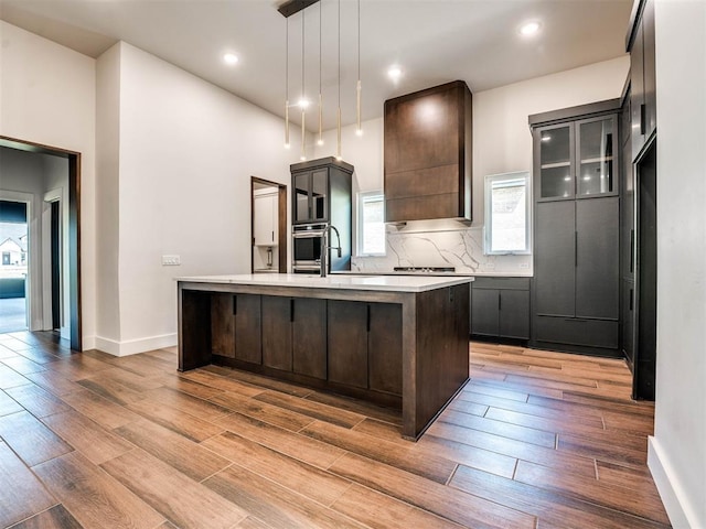 kitchen featuring a center island with sink, oven, decorative light fixtures, and light hardwood / wood-style flooring