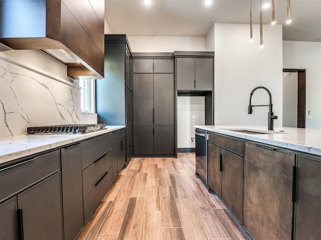 kitchen with appliances with stainless steel finishes, backsplash, light stone counters, sink, and light hardwood / wood-style flooring