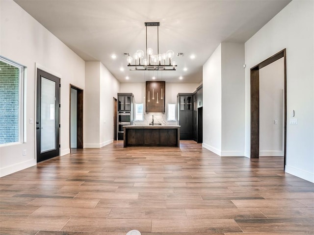 kitchen with hardwood / wood-style floors, a center island with sink, an inviting chandelier, and hanging light fixtures