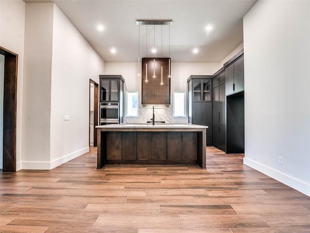 kitchen with a center island with sink, stainless steel oven, and light hardwood / wood-style flooring