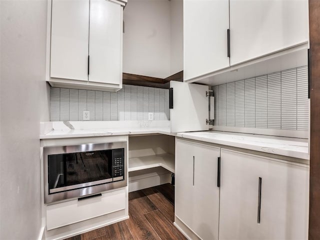 kitchen with stainless steel microwave, dark wood-type flooring, white cabinets, light stone countertops, and fridge