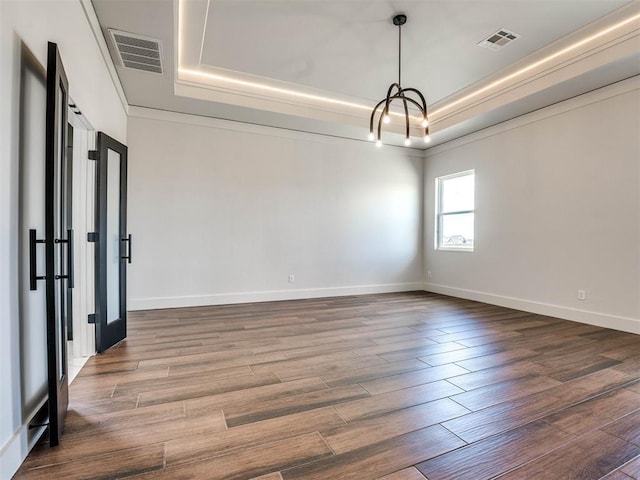 spare room with a tray ceiling, crown molding, dark wood-type flooring, and an inviting chandelier